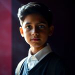 1740650228Volumetric-lighting-rich-burgundy-and-deep-blue.-A-graceful-and-elegant-10-12-year-old-Indian-boy-in-school-uniform-refined-features.-Visible-light-beams-through-dust-or-fog.jpg